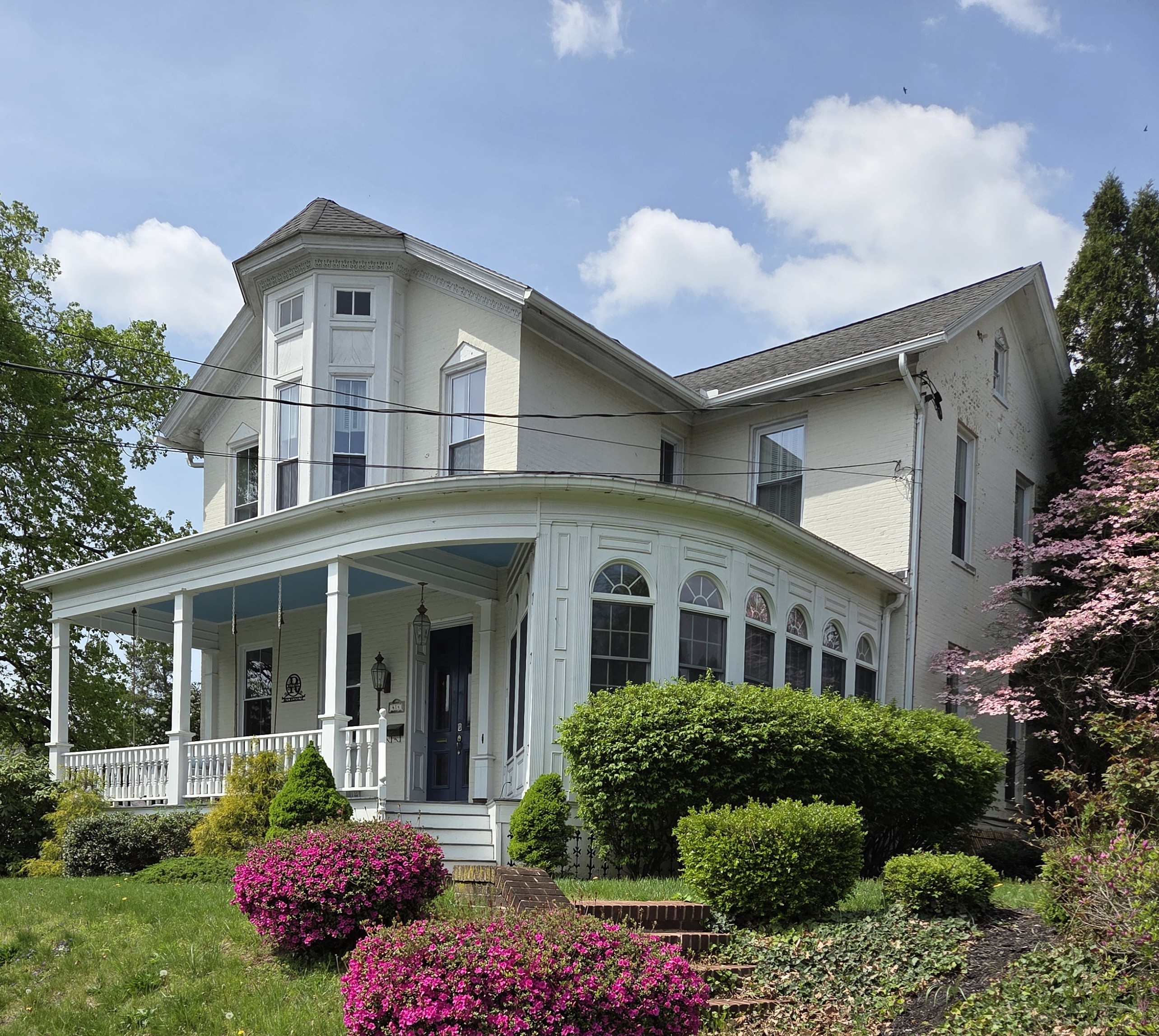 Victorian home with a wrap-around porch and bay windows surrounded by colorful landscaping.