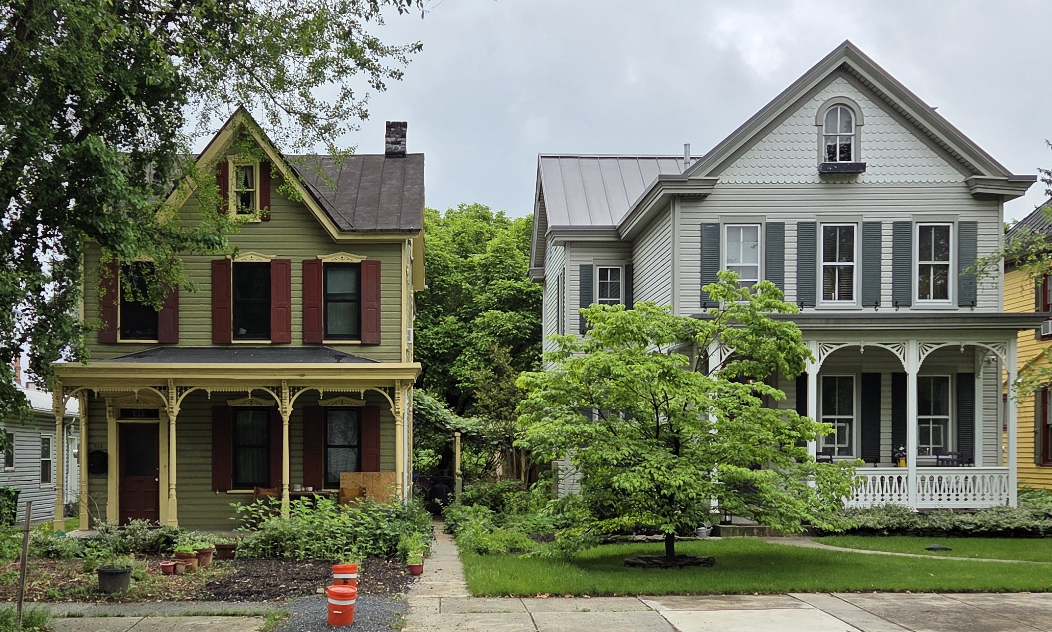Two Victorian-style homes side by side, one with a porch and ornate trim, the other with a gable roof and shutters.