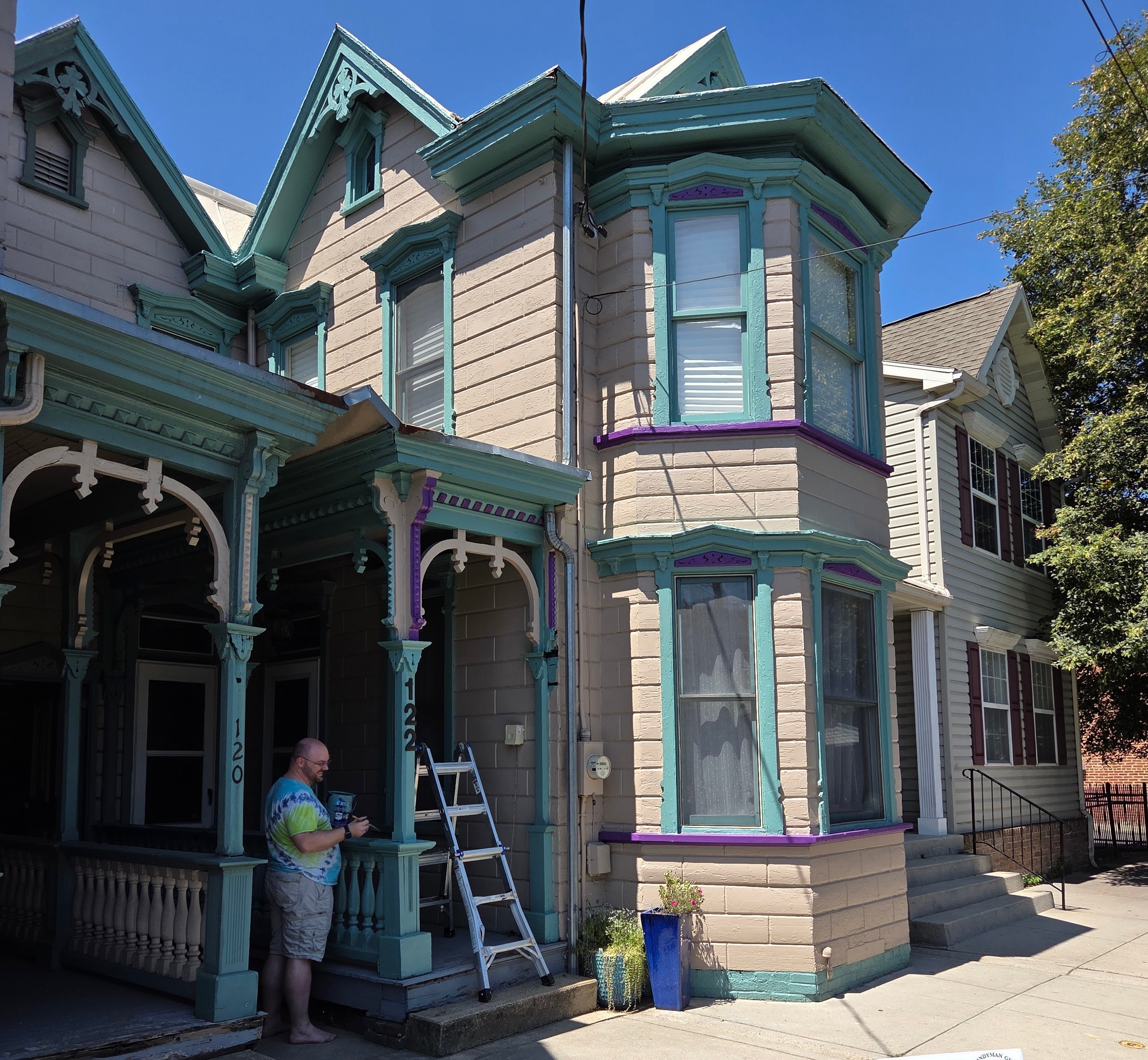 Victorian home with ornate trim, bay windows, and a person painting on the porch.