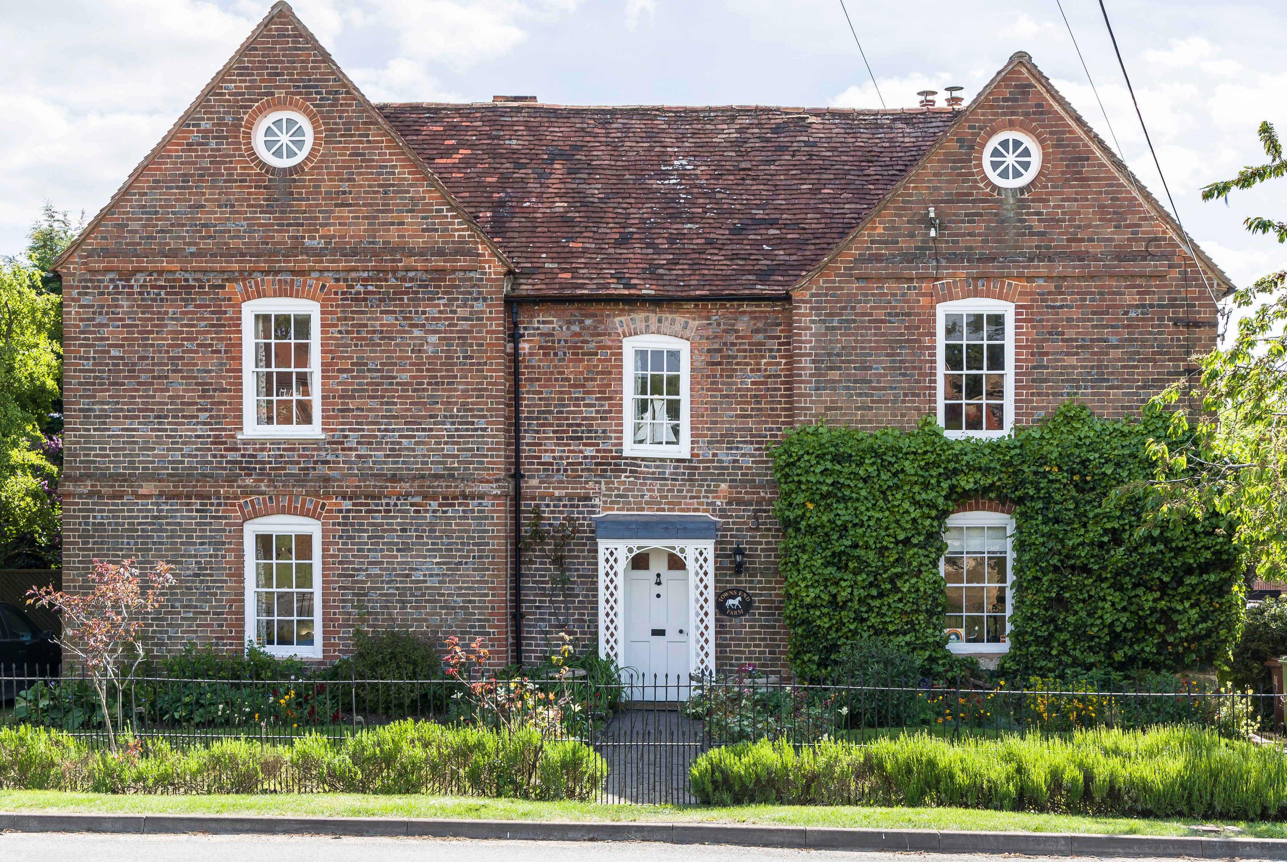 Victorian brick home with a lattice porch and period windows, surrounded by greenery.