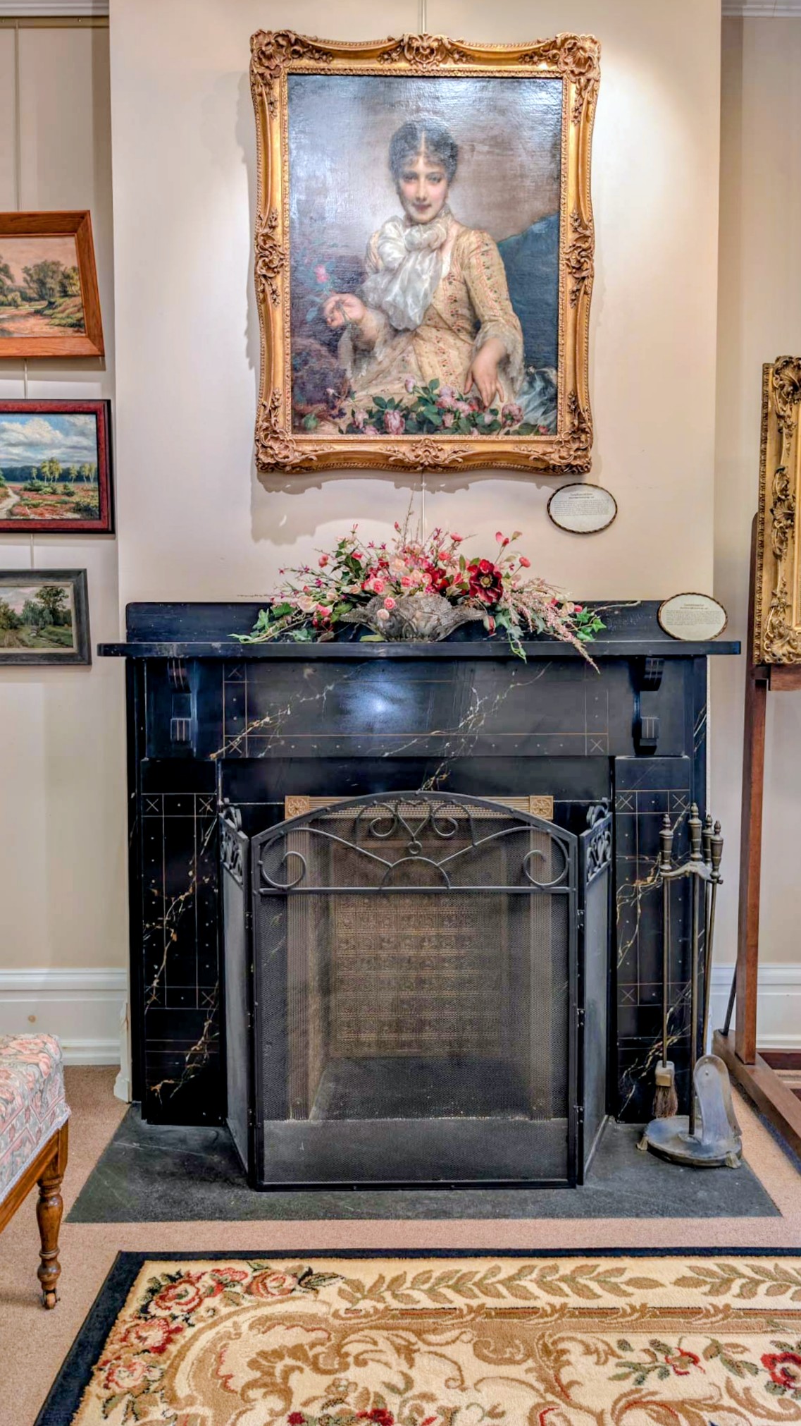 Black marble fireplace with an iron fire screen beneath a gilt-framed portrait of a Victorian lady.