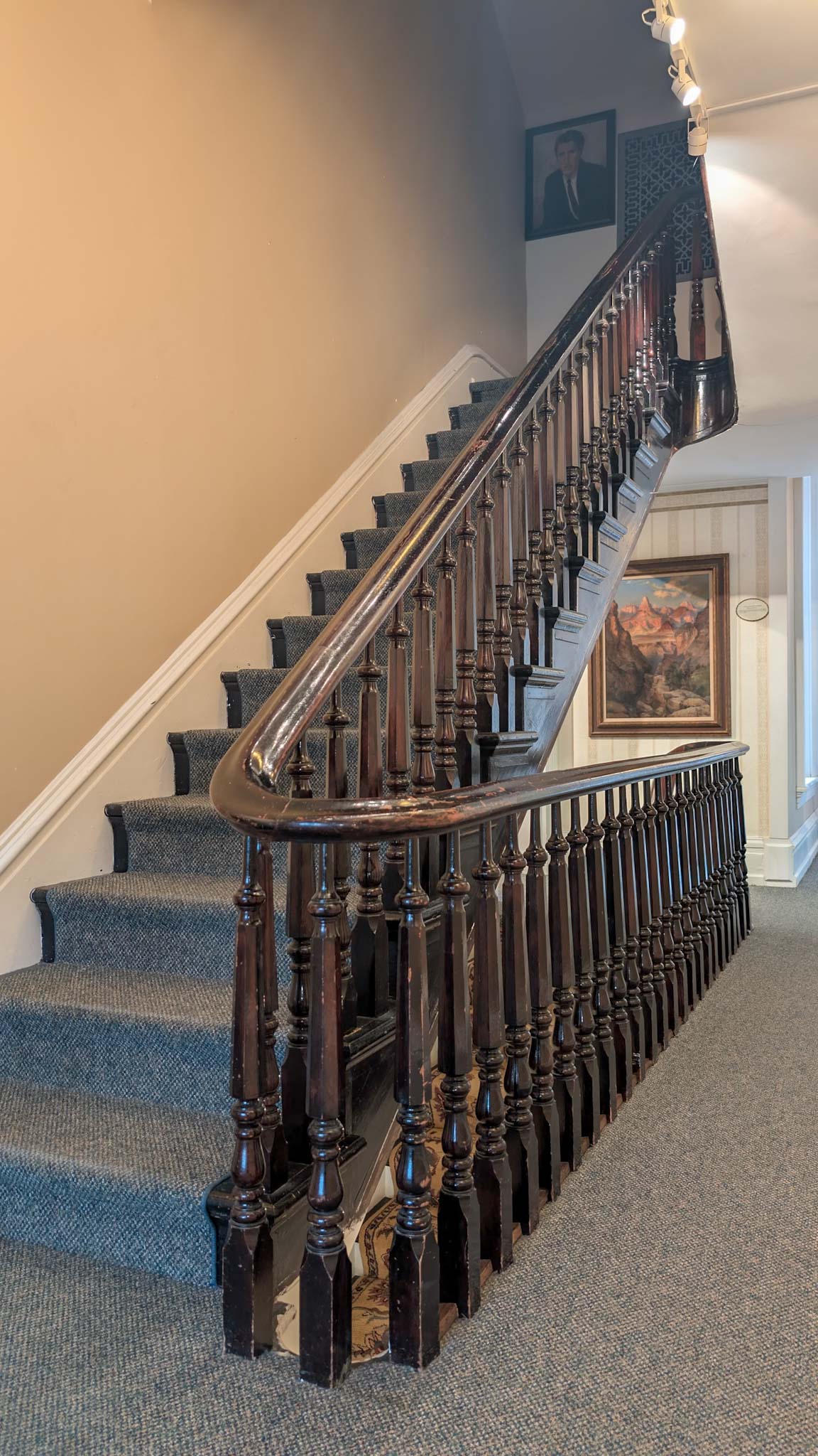 Carved walnut staircase with turned balusters and a carpeted runner rising past framed artwork.