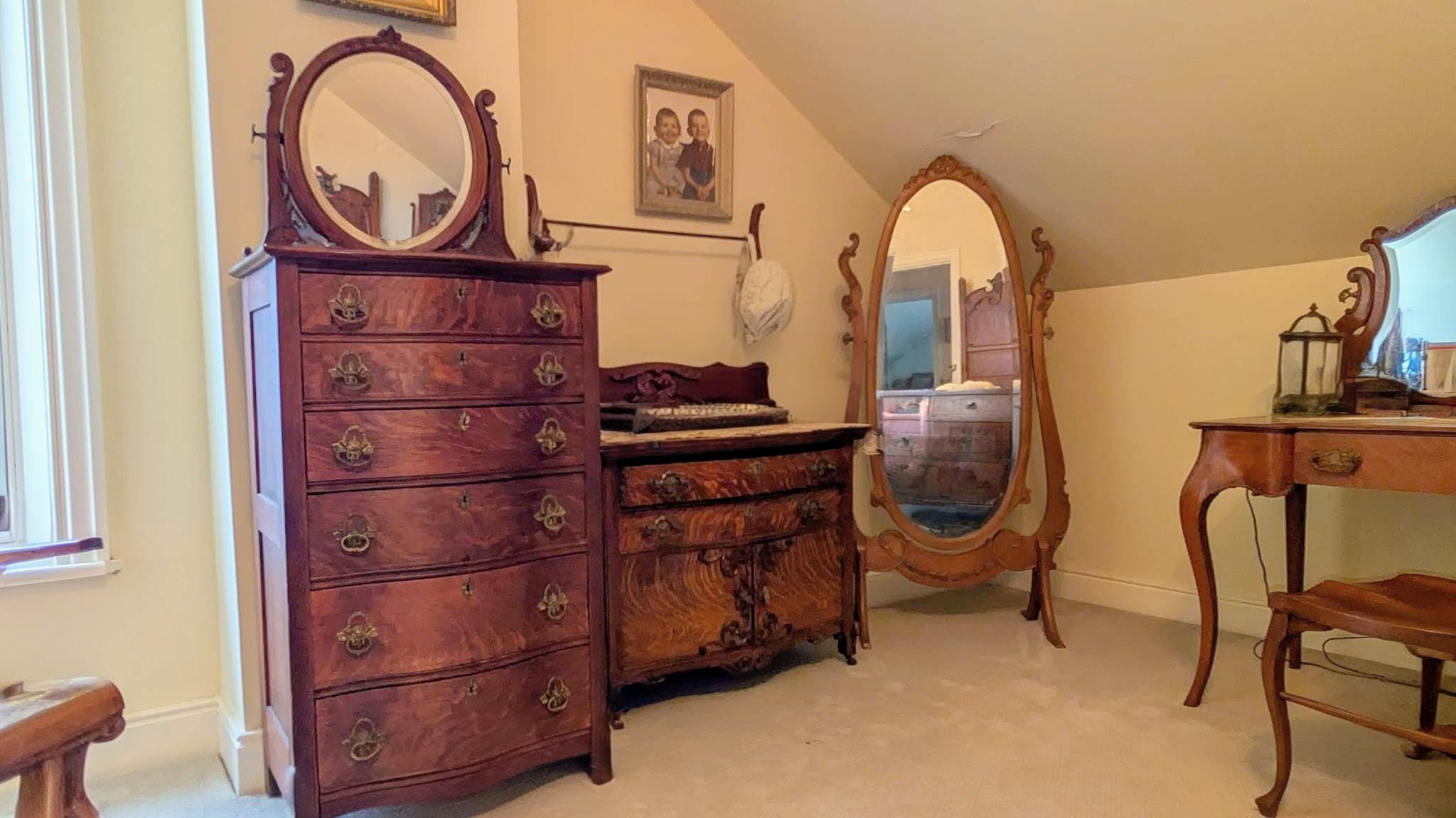 Attic-eave bedroom furnished with an oak highboy, dresser, and oval cheval mirror.