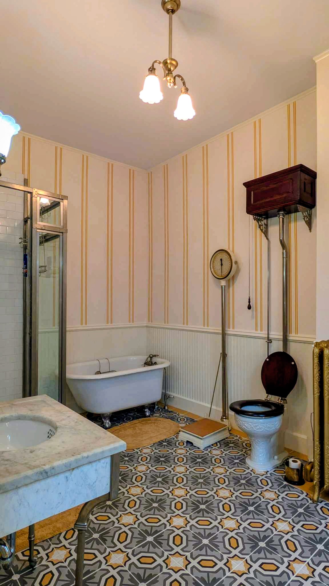 Victorian bathroom with a clawfoot tub, high-tank pull-chain toilet, and patterned encaustic tile floor.