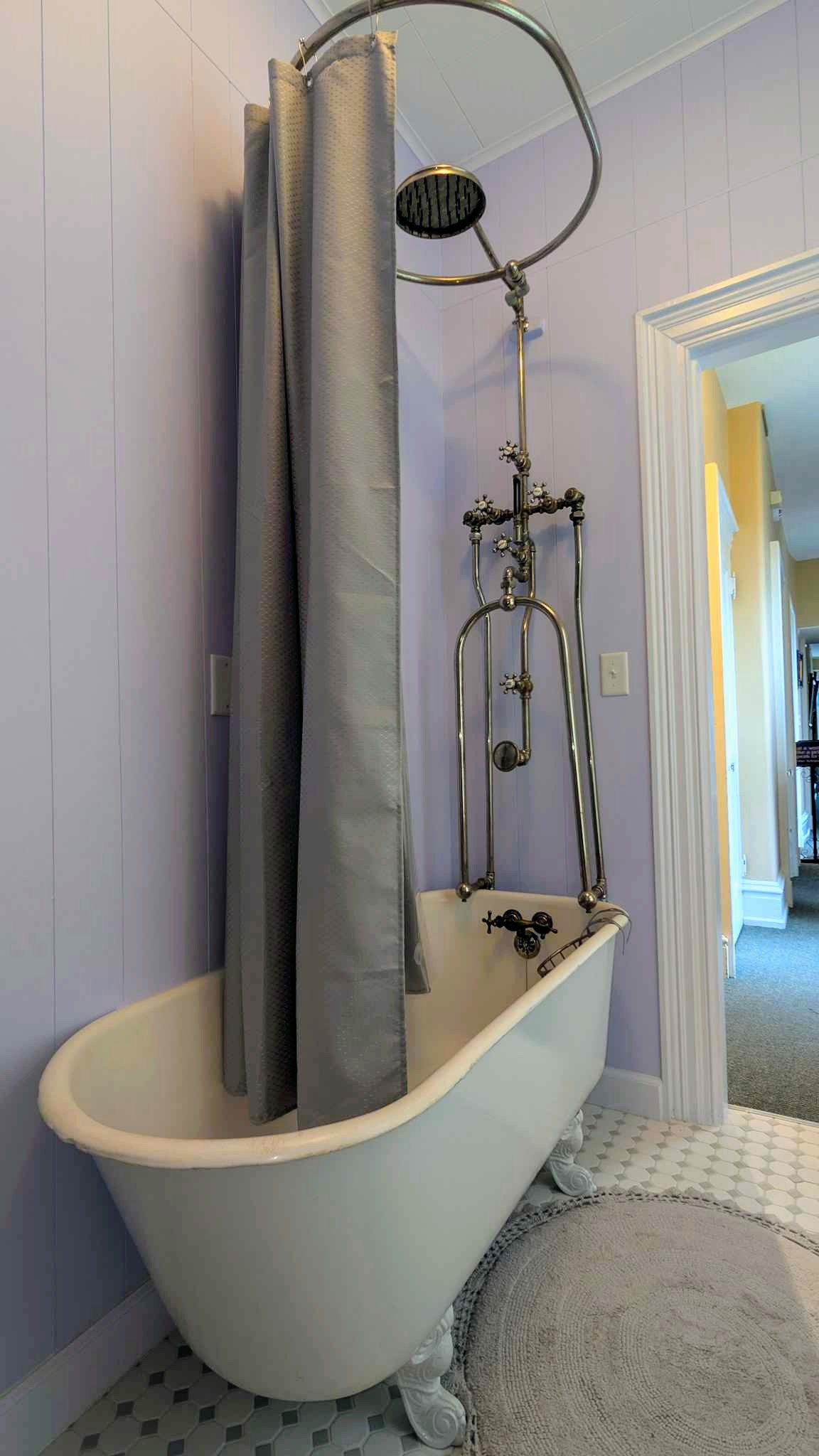 Victorian bathroom with a clawfoot tub, high-tank pull-chain toilet, and patterned encaustic tile floor.
