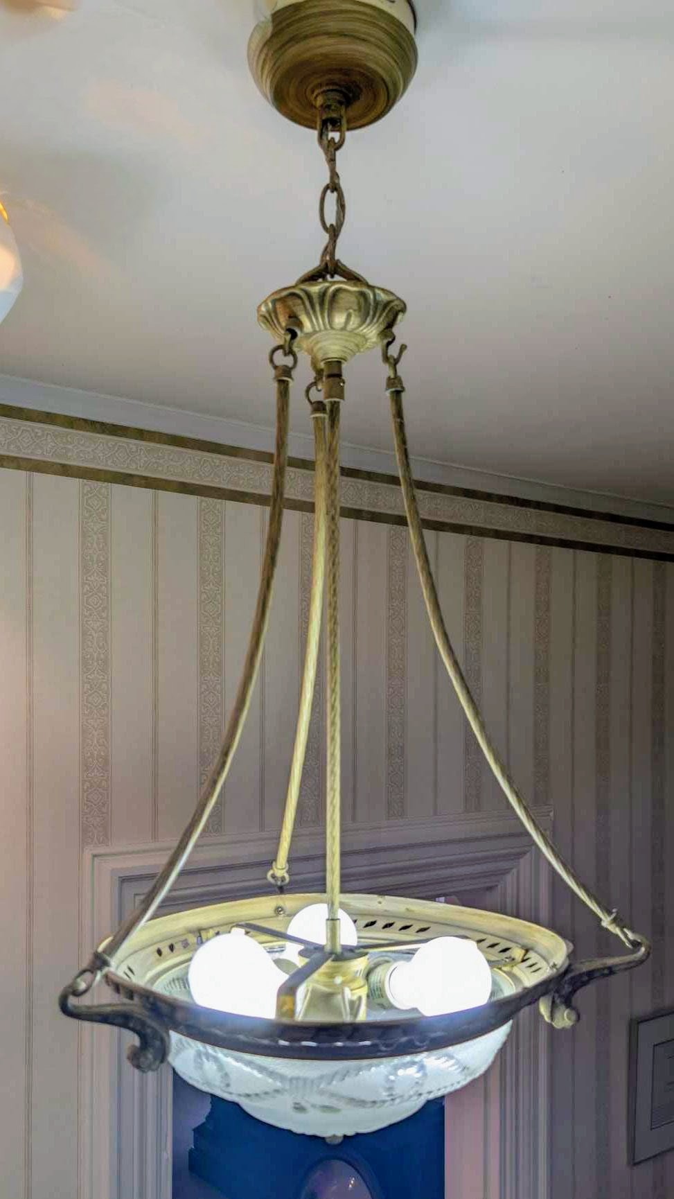 Antique brass pendant light with a frosted-glass inverted dome shade against striped wallpaper.
