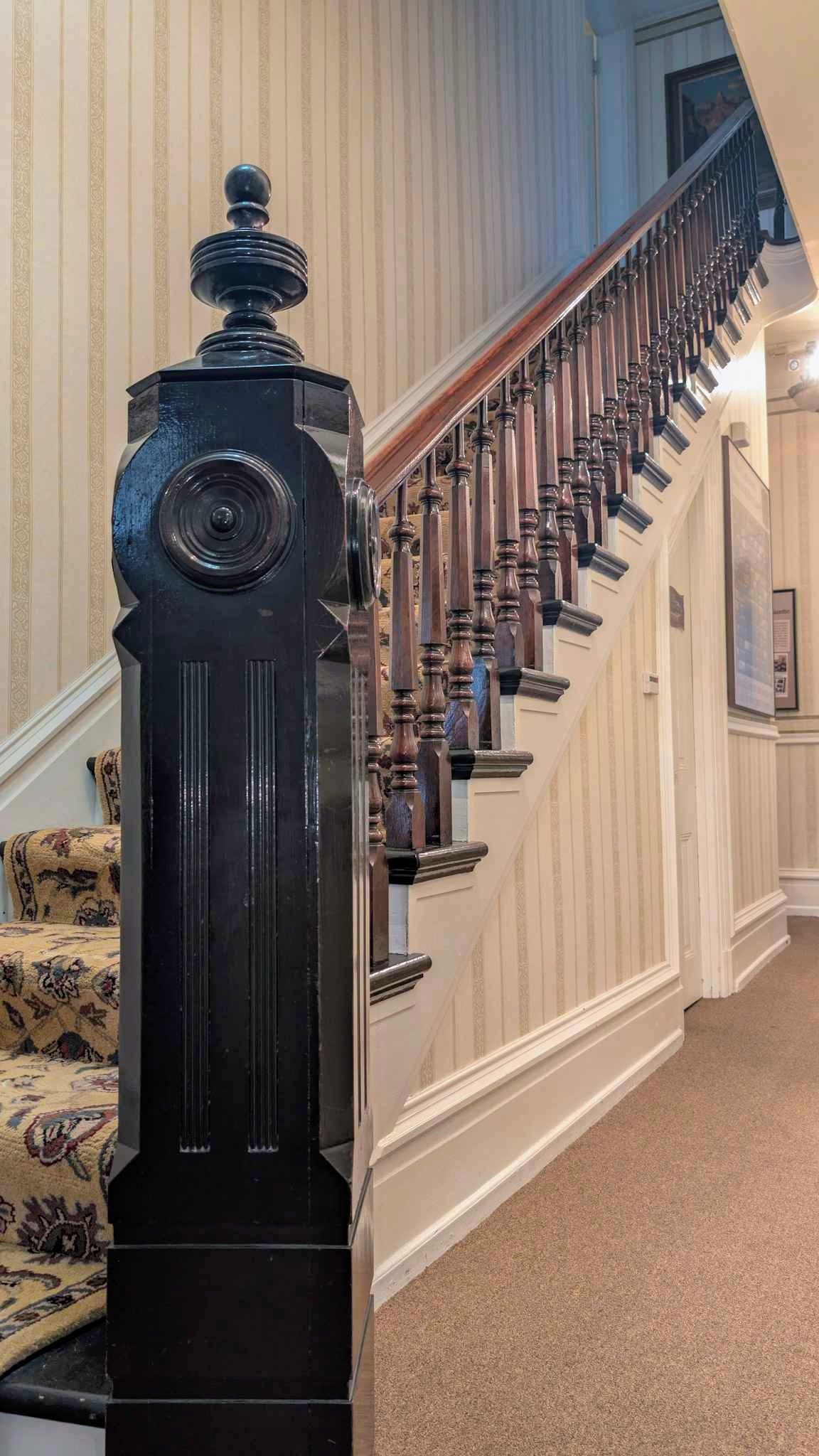 Ornate black newel post with a turned finial anchoring the walnut staircase.