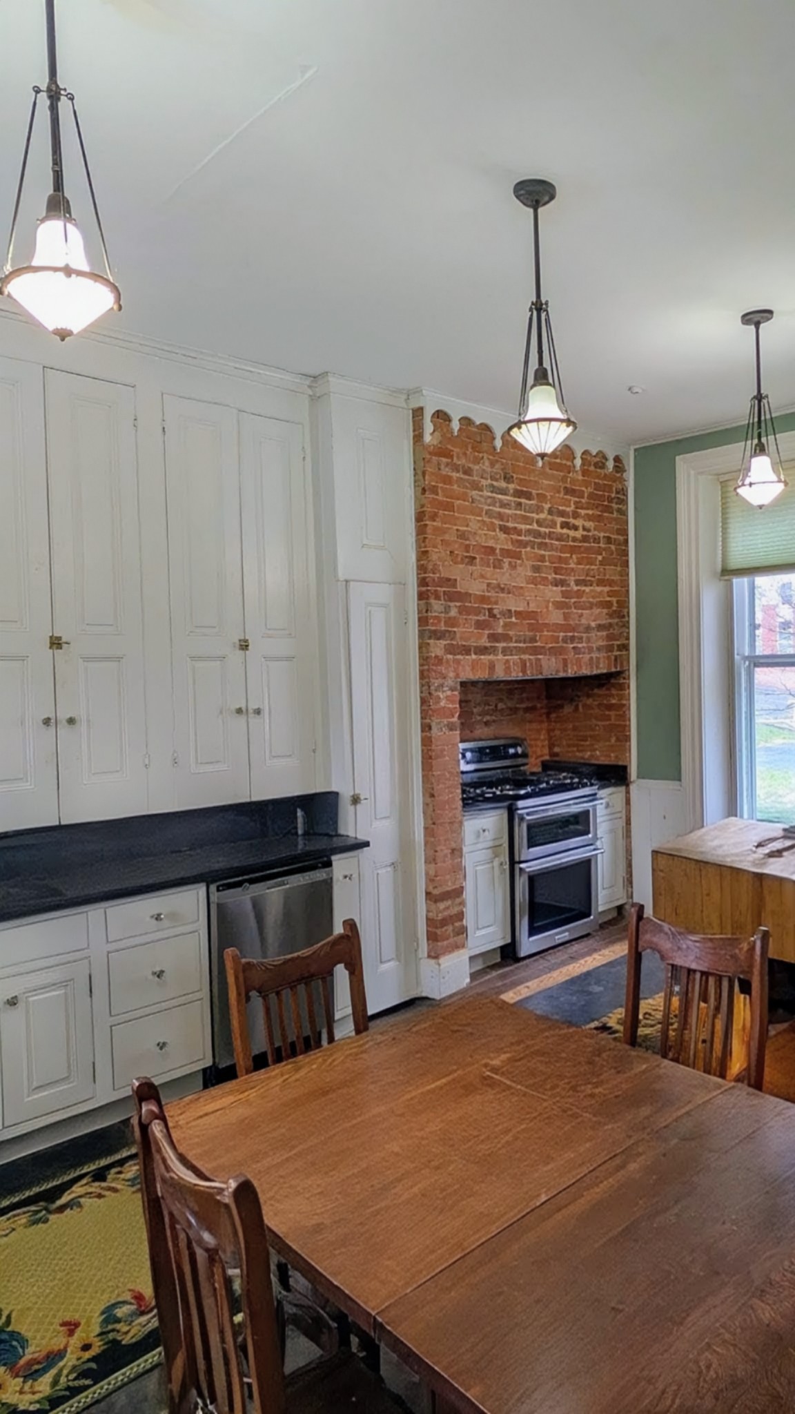 Kitchen with white cabinetry and an exposed-brick chimney breast above a stainless range, set with an oak table.