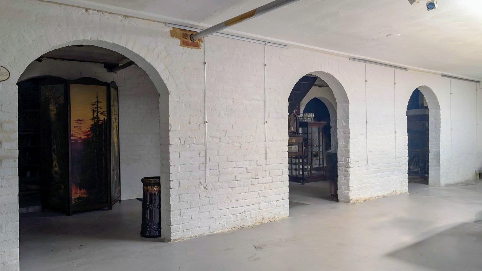 Whitewashed brick lower level with a row of arched openings and a painted folding screen.