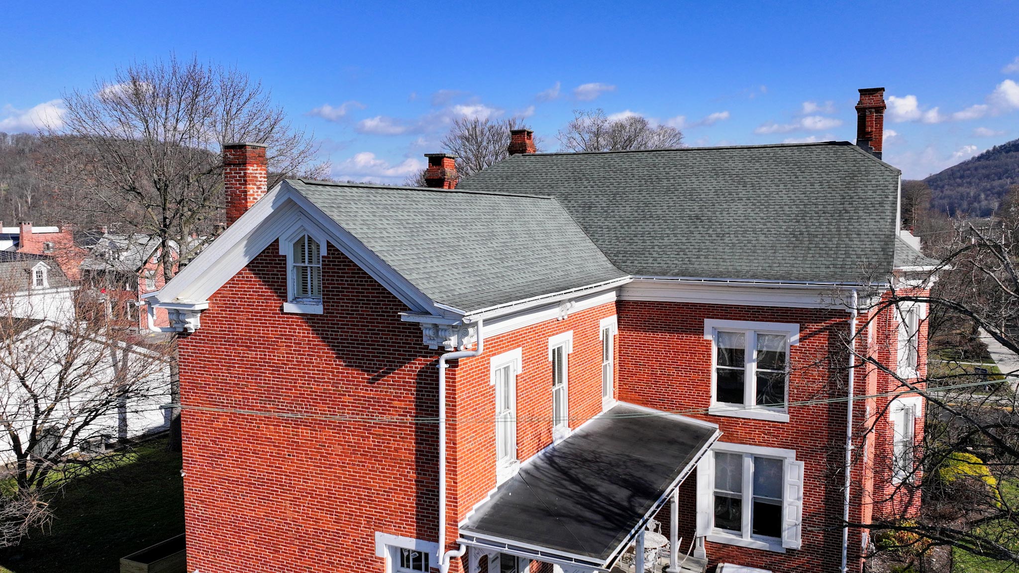 Elevated view of the red-brick mansion's gabled roofline and brick chimneys above Bedford's rooftops.