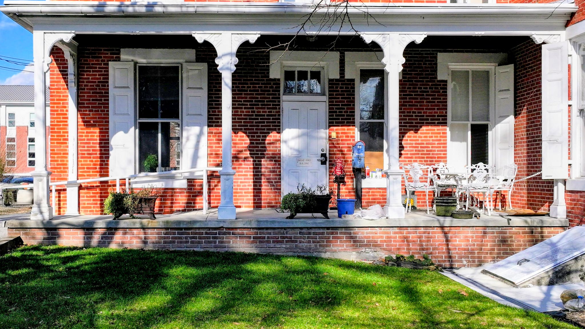 The brick mansion's covered front porch with scroll-bracketed columns and a white entry door.