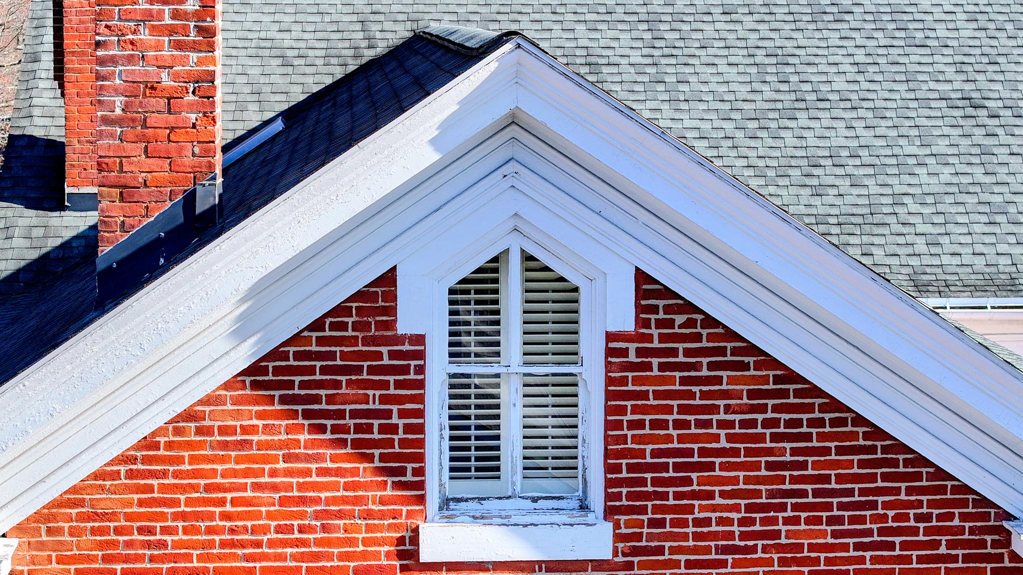 Gable peak with a pointed-arch louvered attic window set in red brick with white trim.