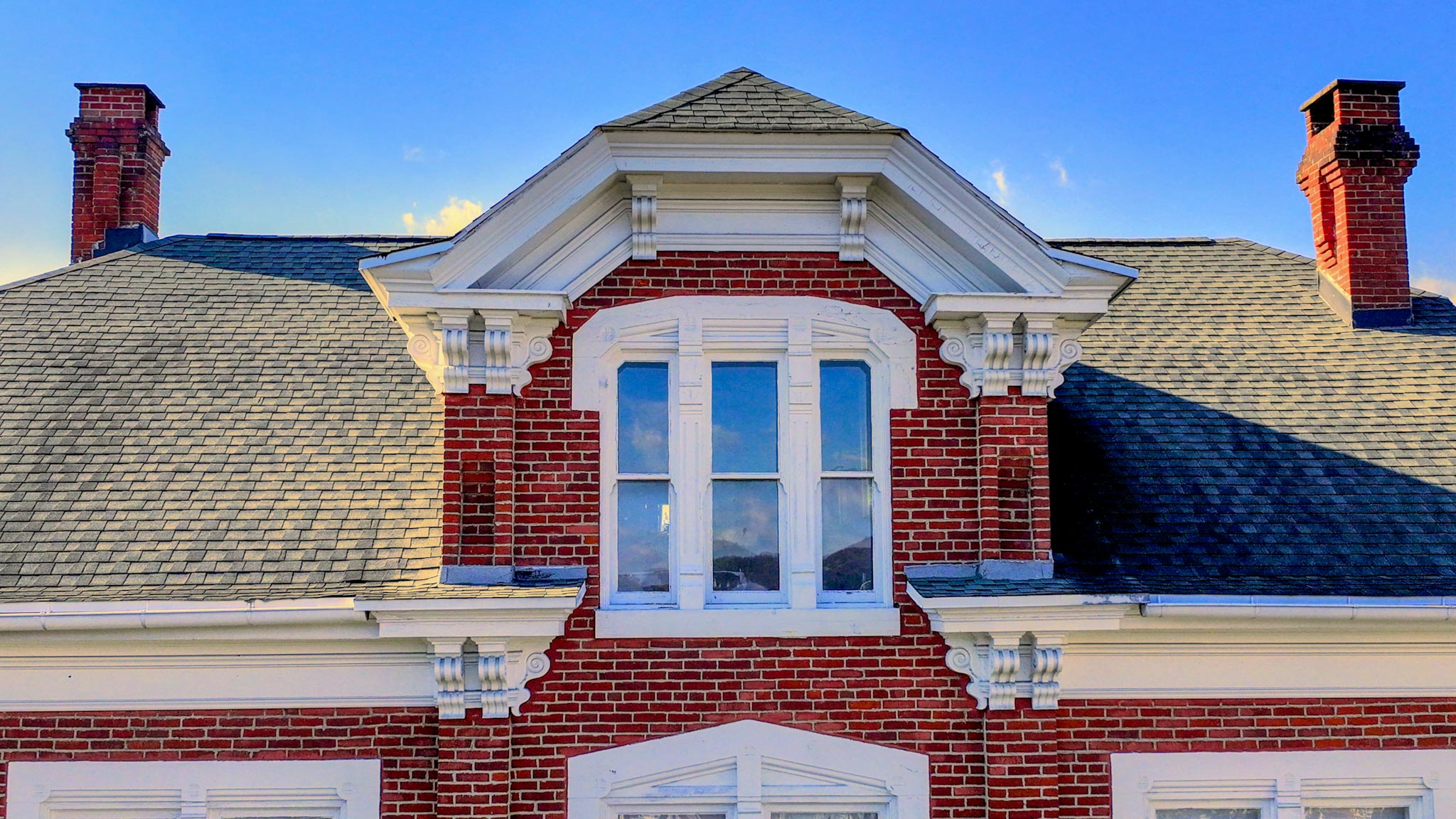 Central gabled dormer with paired windows and bracketed pediment between two brick chimneys.