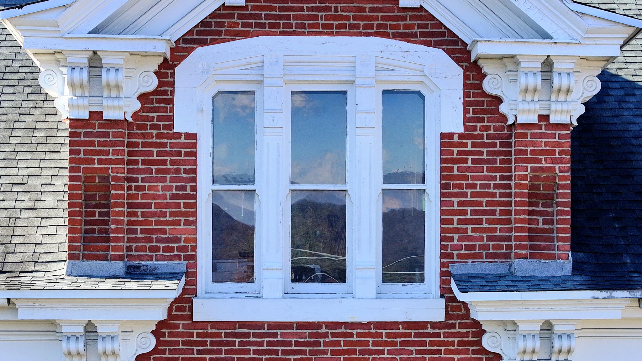 Arched double window with a carved white surround, the ridgeline reflected in its panes.
