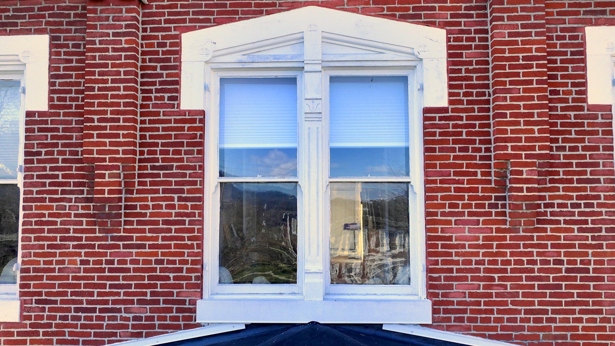 Window with a carved white keystone surround and central pilaster in the red-brick wall.