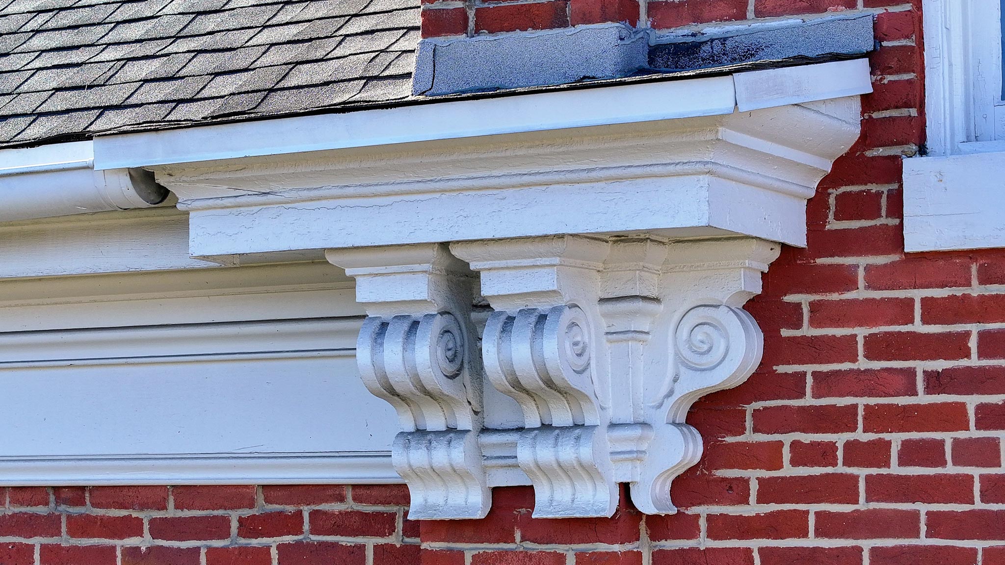 Ornate scrolled cornice brackets beneath the eaves against the red-brick wall.