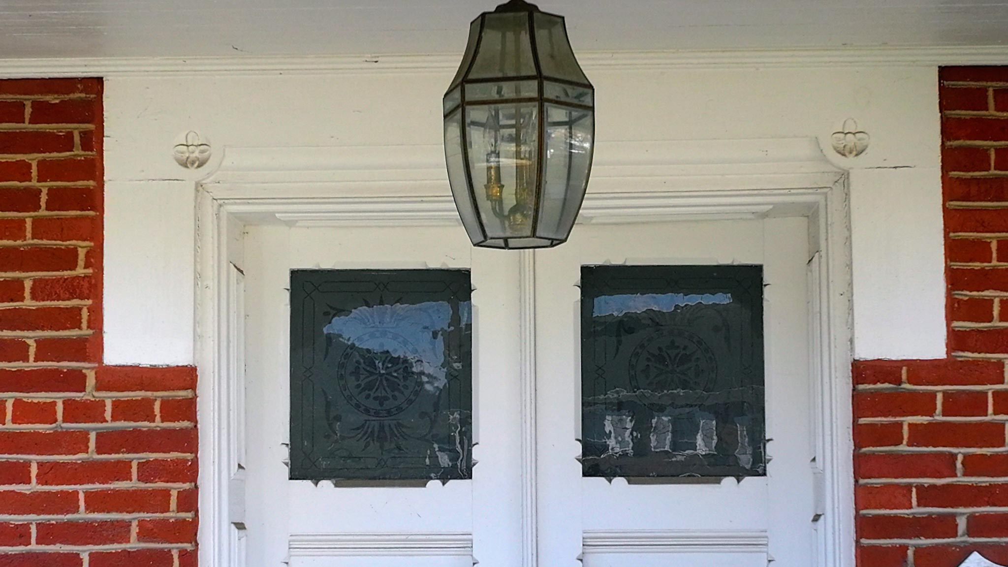 Hanging glass lantern above the front doors' etched-glass panels on the brick porch.