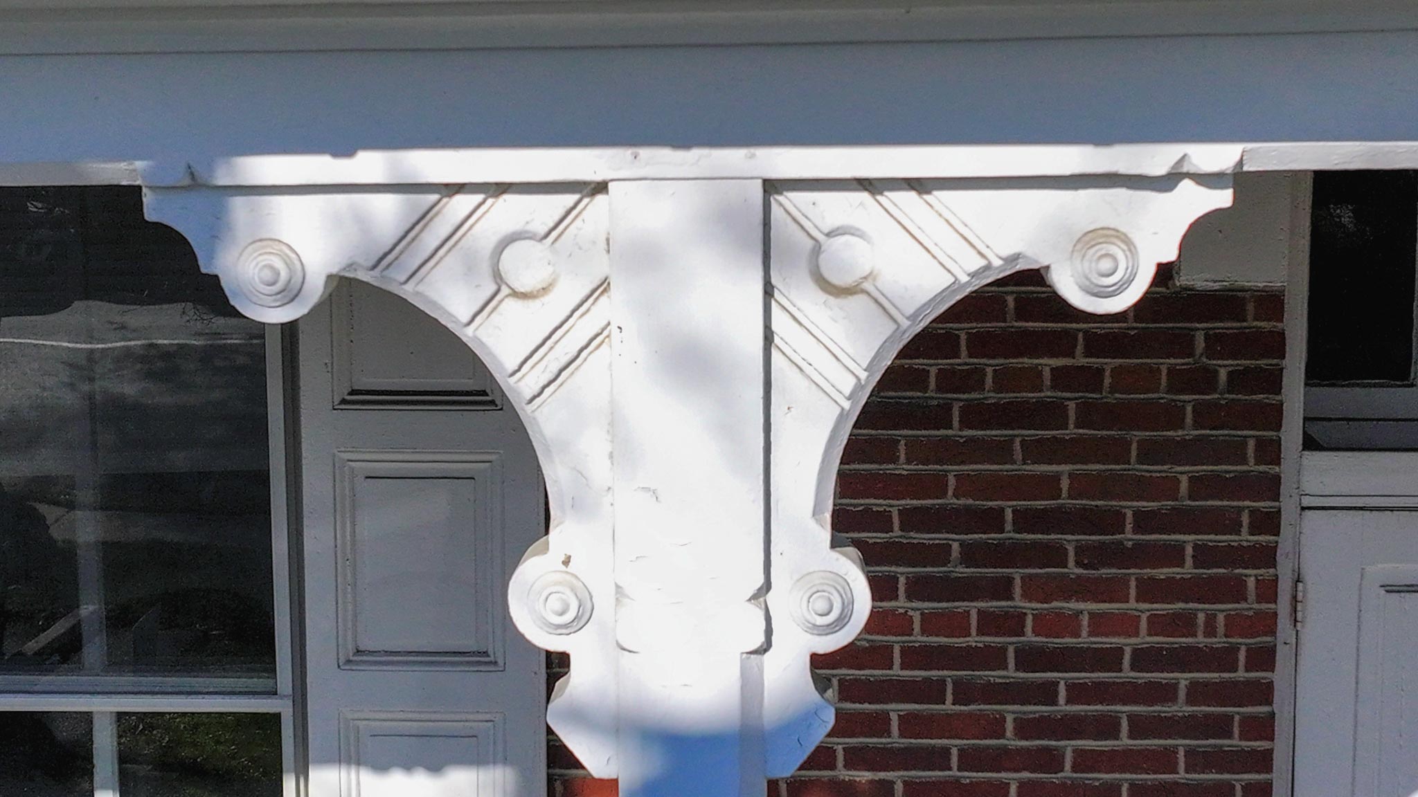 Decorative scroll-cut porch spandrels between the columns above the brick wall.