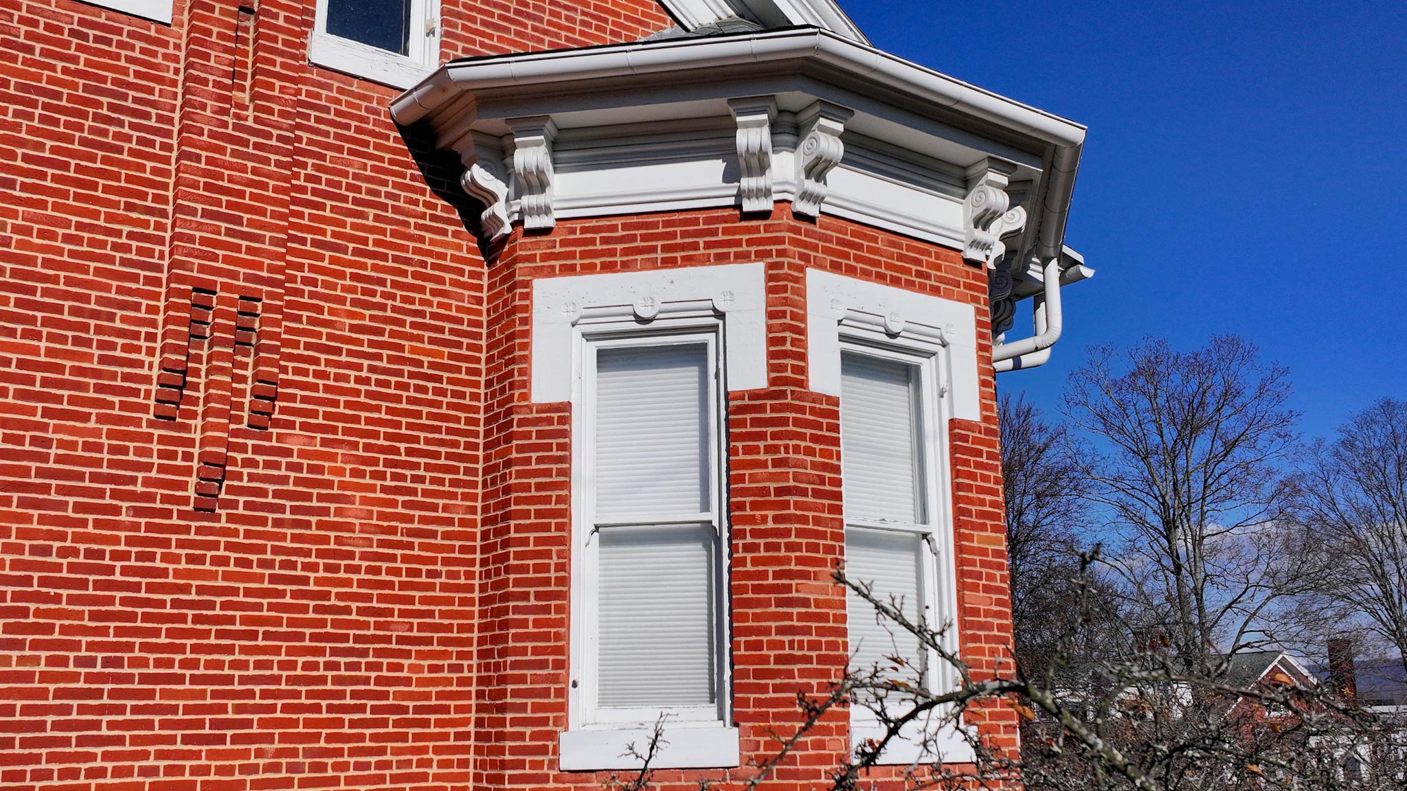 Projecting brick bay with a bracketed cornice and white-trimmed windows against a blue sky.