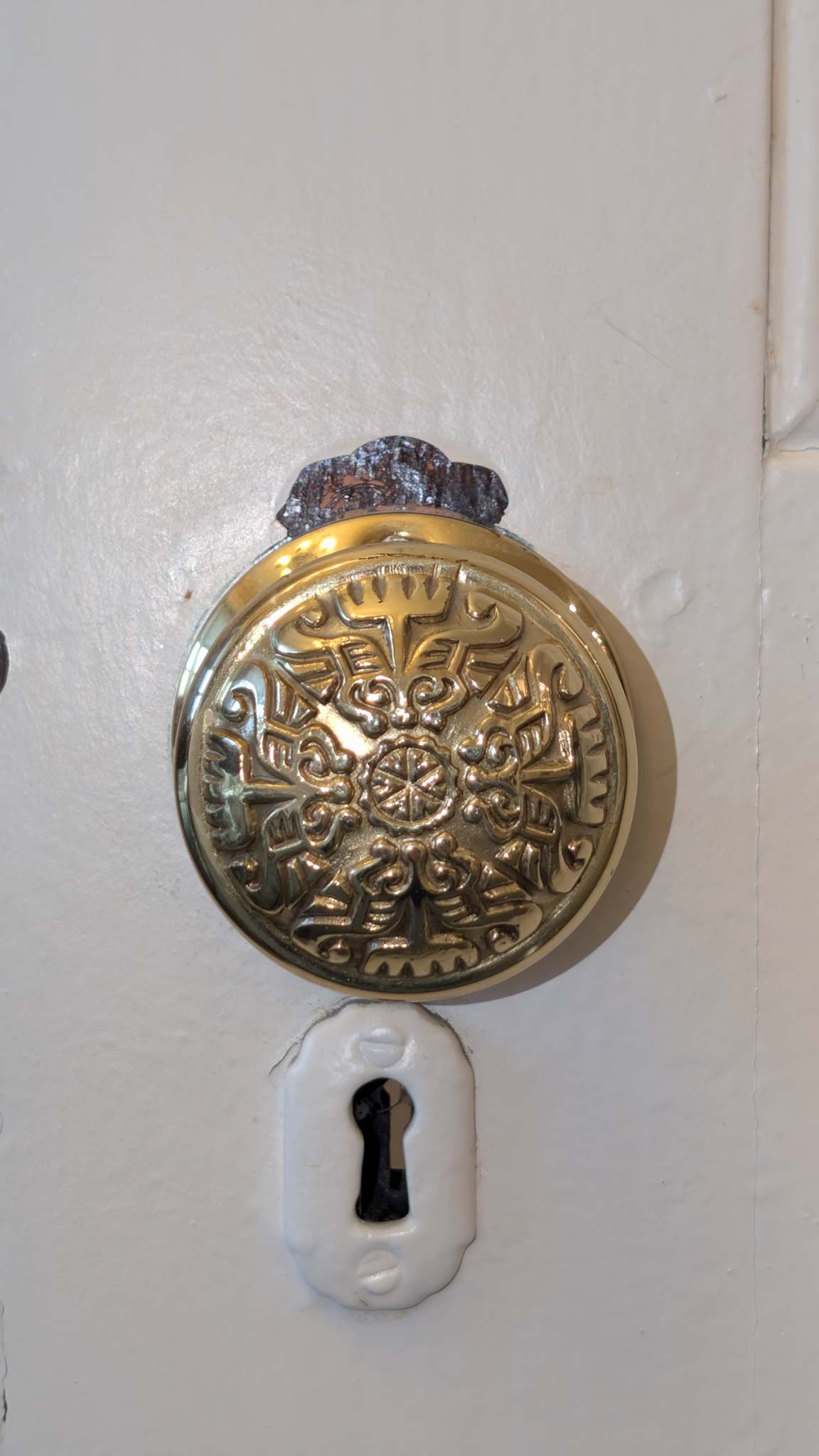 Ornate cast-brass doorknob with a floral relief above a porcelain keyhole escutcheon.