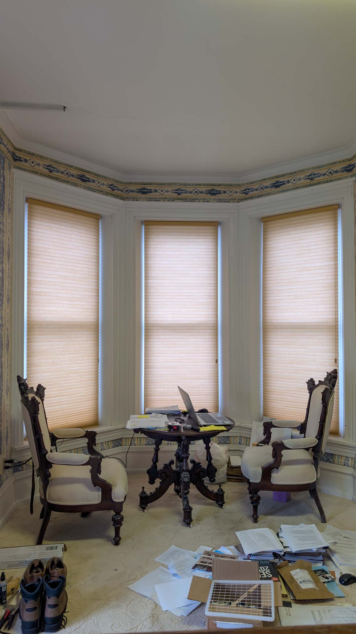 Bay-window turret room with carved Victorian parlor chairs and a marble-top table beneath a painted frieze.