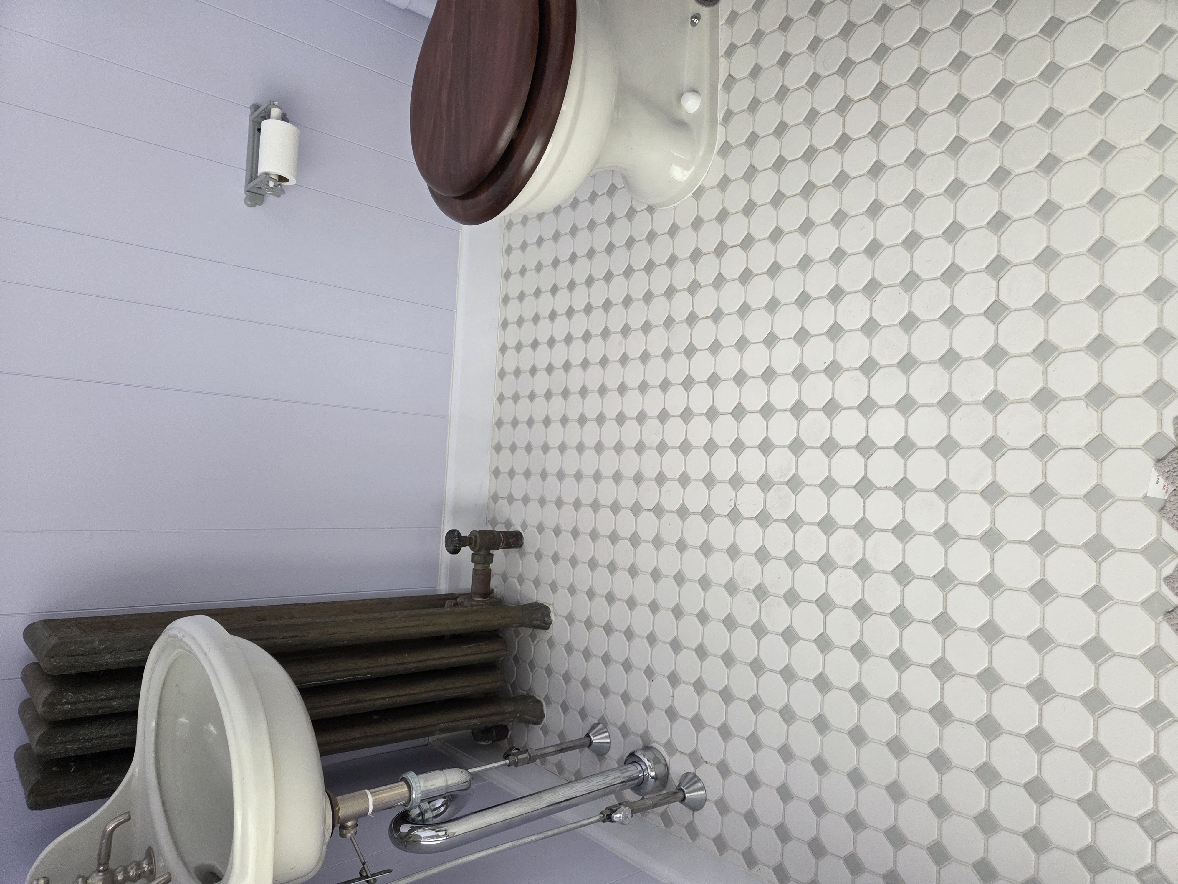 Victorian bathroom with a pedestal sink, wooden toilet seat, hexagonal tile flooring, and a radiator.