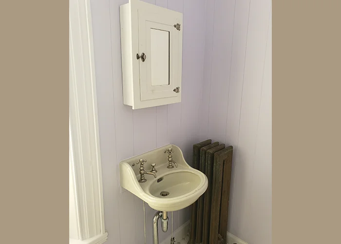 Victorian bathroom with a vintage sink, ornate faucets, and a medicine cabinet against lavender walls.