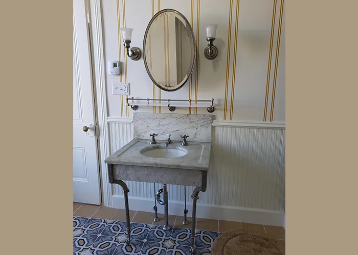 Victorian bathroom showcasing a marble sink, vintage faucets, and wall sconces.