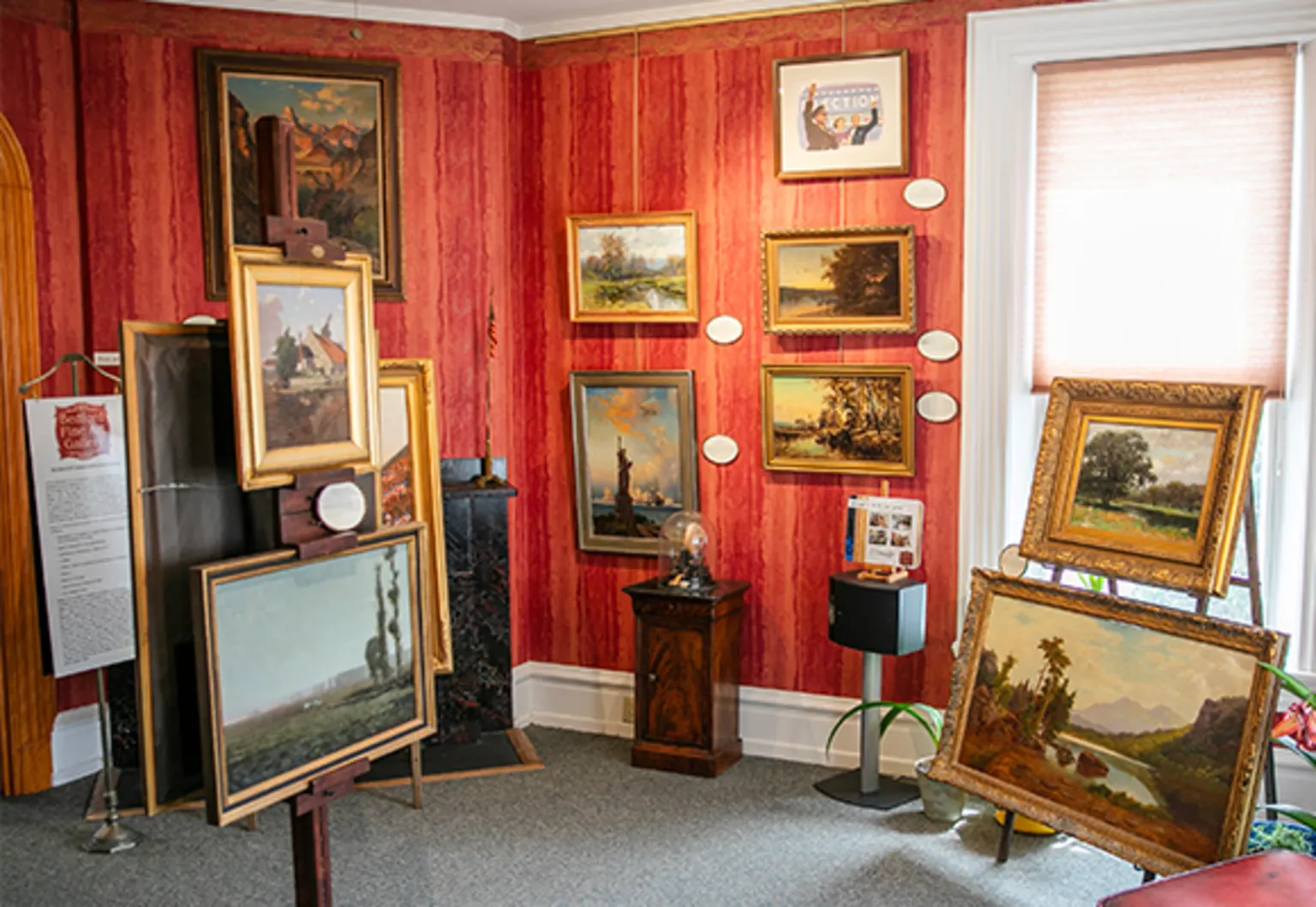 A red-walled gallery room hung and stacked with original 19th-century paintings in gold frames